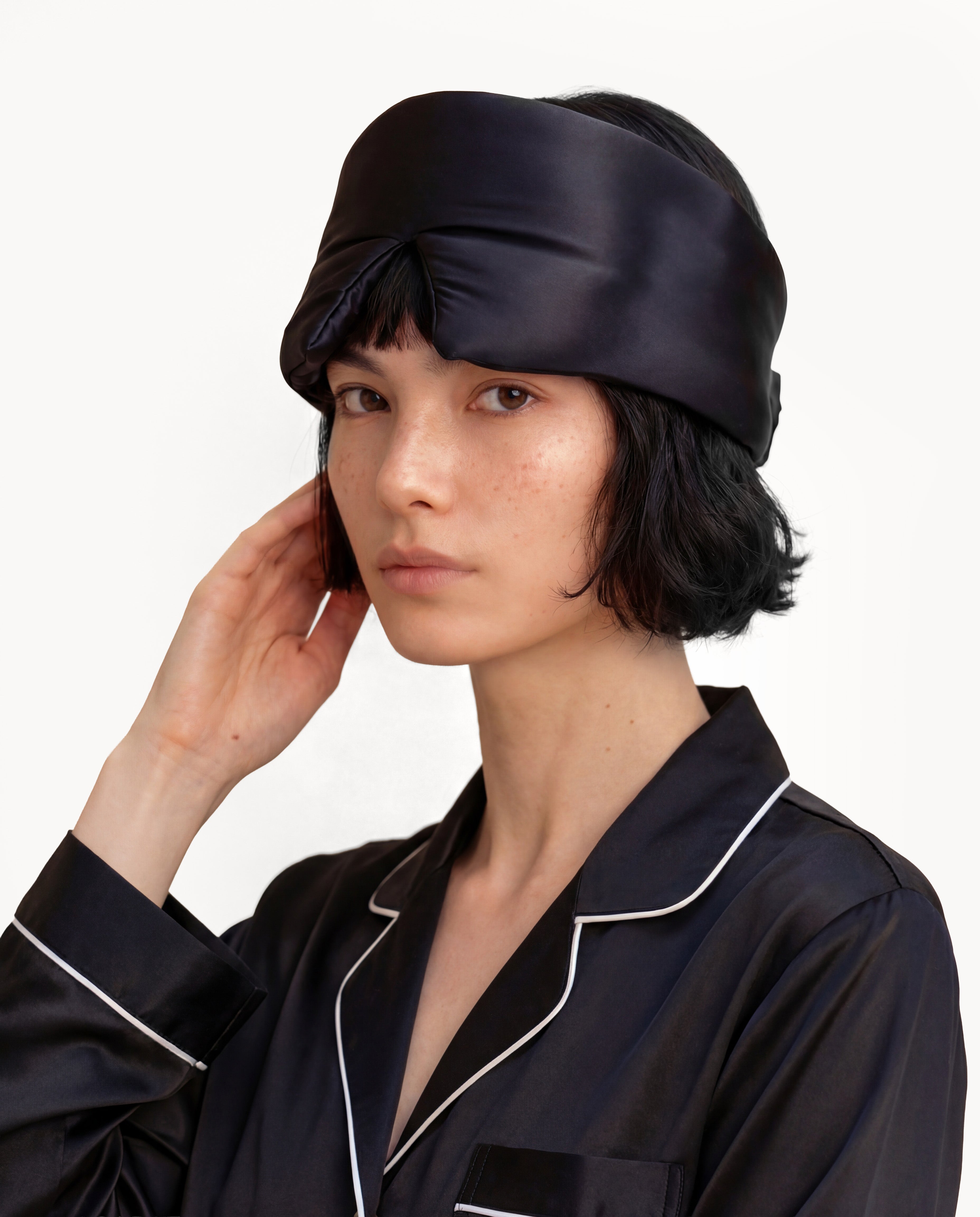 Model with a Black NORA silk sleep mask on her forehead, handcrafted from real silk mulberry silk fabric for a luxury aesthetic.